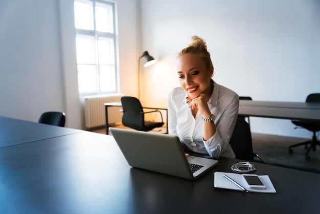 Jonge vrouw die bij het moderne bureau met laptop werkt