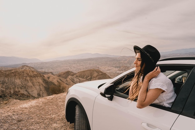 Jonge vrouw die bij zonsondergang vanuit haar auto een prachtig woestijnlandschap bewondert