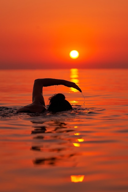 Jonge vrouw die bij zonsopgang in de zee zwemt