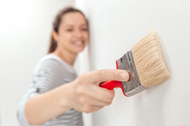 Jonge vrouw die binnenlandse muur met verfborstel schildert