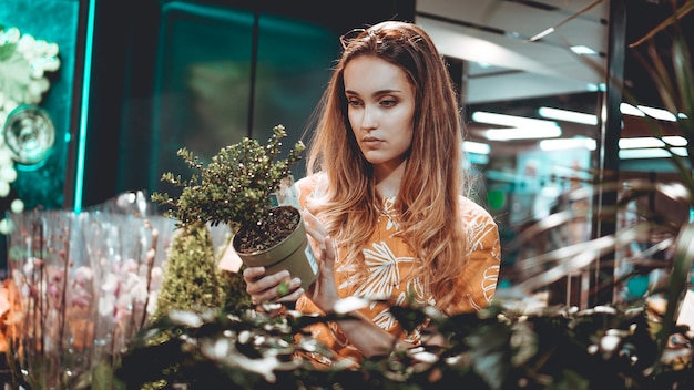 Jonge vrouw die bloemen in een pot bij een tuincentrum koopt