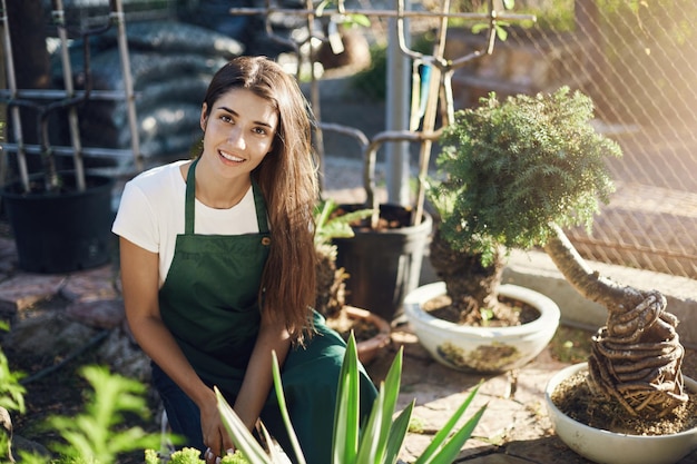 Jonge vrouw die bonsaibomen verzorgt die zich voorbereiden om ze in nieuwe kommen te verplaatsen, tuinman werkt op zijn best Kijkend naar de camera die lacht