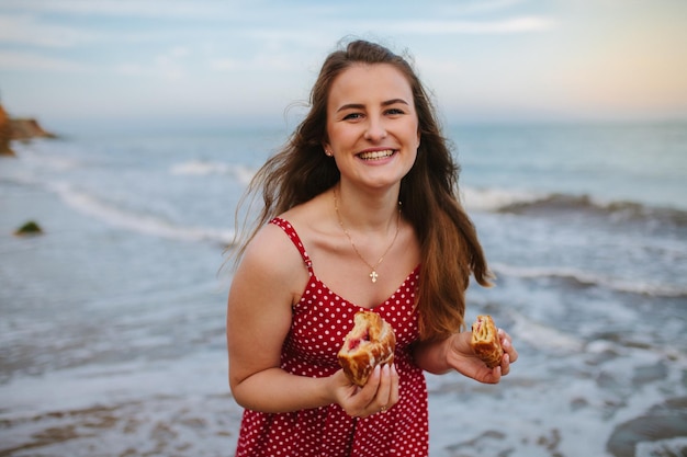 Jonge vrouw die buiten een croissantmaaltijd eet Mooi meisje aan het ontbijt aan zee, oceaan Zomerplezier