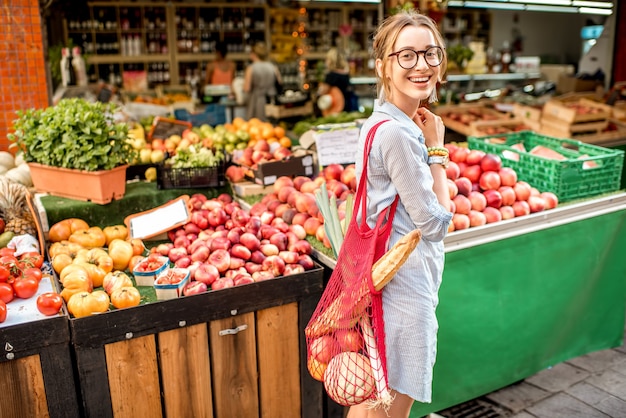 Jonge vrouw die buiten staat met een netzak vol verse groenten voor de voedselmarkt