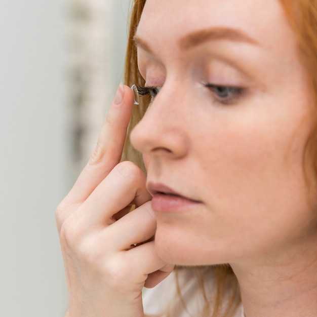 Foto jonge vrouw die contactlens in haar oog zet