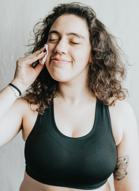 Foto jonge vrouw die cosmetische katoenen schijf vasthoudt en gebruikt terwijl ze ontspannen en glimlachend close-up portret in studio is