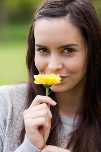 Jonge vrouw die de camera bekijkt terwijl het ruiken van een gele bloem