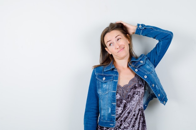 Jonge vrouw die de hand op het hoofd houdt in een spijkerjasje, jurk en er verward uitziet. vooraanzicht.