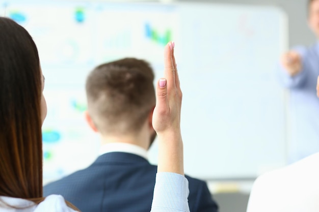 Jonge vrouw die de hand opsteekt om een vraag te stellen bij indoor business training close-up