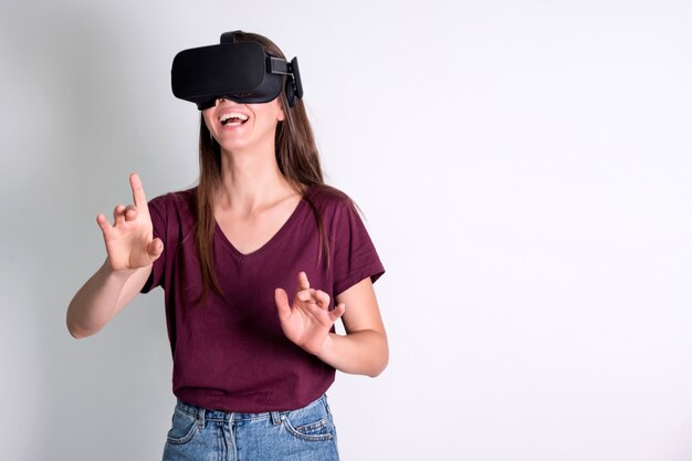 Jonge vrouw die de hoofdtelefoon van virtuele werkelijkheidsbeschermende brillen, vr doos draagt. verbinding, technologie, nieuwe generatie, voortgangsconcept. meisje probeert objecten in virtual reality aan te raken. studio geschoten op grijs