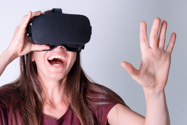 Jonge vrouw die de hoofdtelefoon van virtuele werkelijkheidsbeschermende brillen, vr doos draagt. verbinding, technologie, nieuwe generatie, voortgangsconcept. meisje probeert objecten in virtual reality aan te raken. studio geschoten op grijs