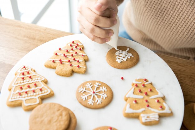 Jonge vrouw die de koekjes van peperkoekkerstmis verfraaien met koninklijk suikerglazuur