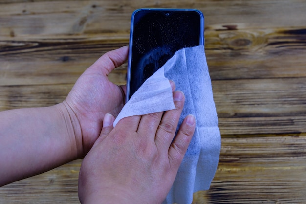 Jonge vrouw die de weergave van haar smartphone schoonmaakt met het natte doekje