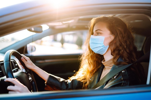 Jonge vrouw die een auto bestuurt met een medisch masker op tijdens een epidemie Transportisolatie Covid2019