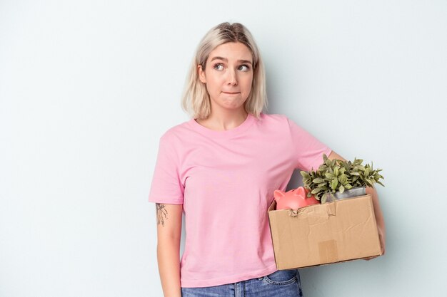 Jonge vrouw die een beweging maakt over een geïsoleerde achtergrond verward, voelt zich twijfelachtig en onzeker.