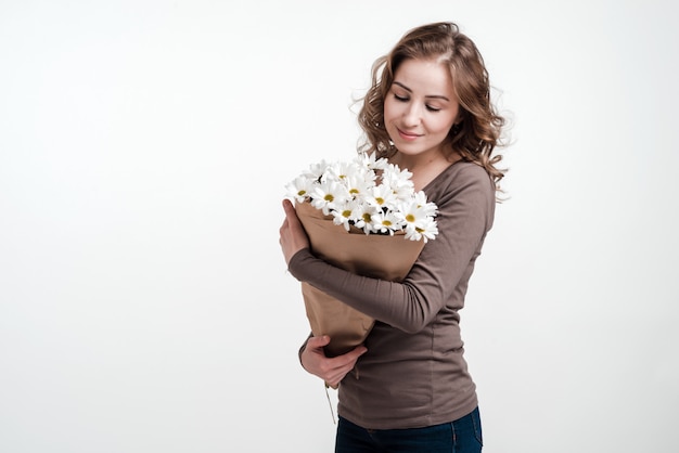 Jonge vrouw die een boeket van margrieten houdt. Witte muur.