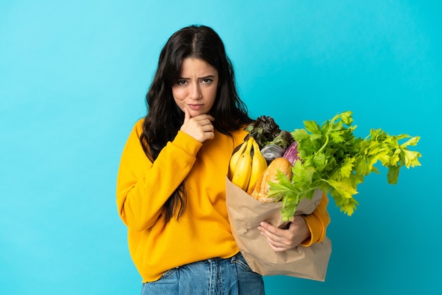 Jonge vrouw die een boodschappentas houdt die bij het blauwe denken wordt geïsoleerd