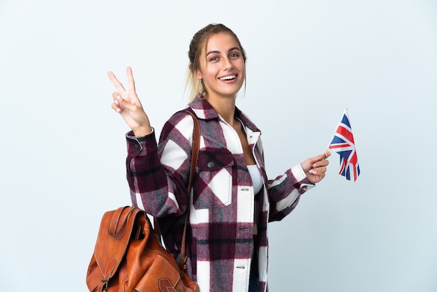 Jonge vrouw die een Britse vlag houdt die op witte achtergrond wordt geïsoleerd die en overwinningsteken glimlacht toont