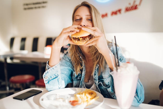 Jonge vrouw die een burger eet in een restaurant.