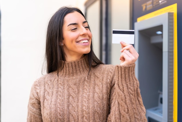 Foto jonge vrouw die een creditcard vasthoudt en naar buiten kijkt terwijl ze glimlacht