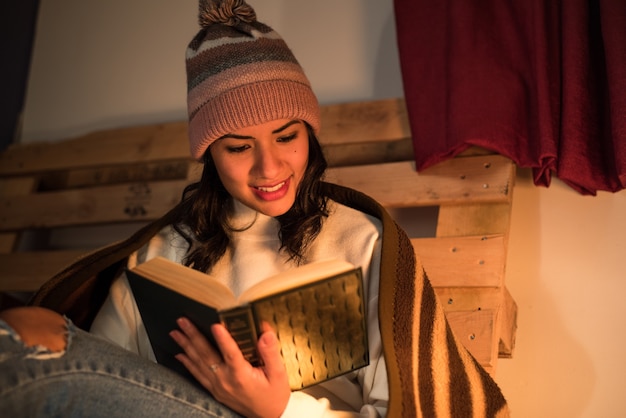 Jonge vrouw die een de winterhoed draagt die een boek leest met een erachter pallet