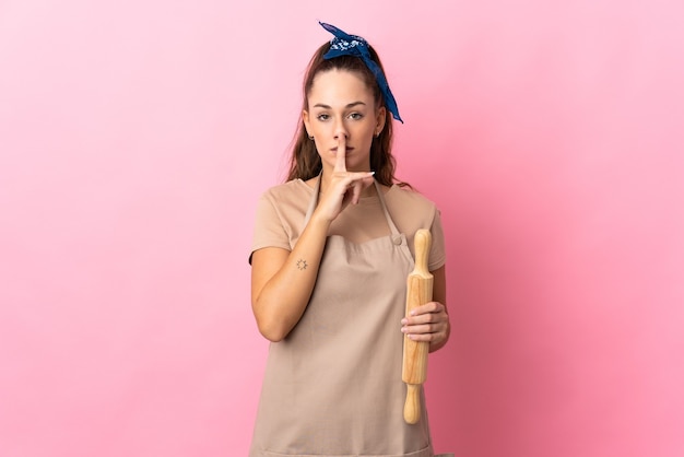 Jonge vrouw die een deegroller vasthoudt met een teken van stiltegebaar dat de vinger in de mond steekt