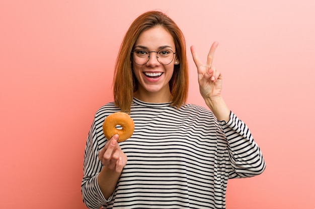 Jonge vrouw die een doughnut houdt die nummer twee met vingers toont.