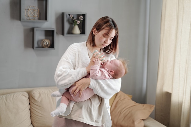 Jonge vrouw die een flesje vasthoudt terwijl ze haar dochtertje voedt