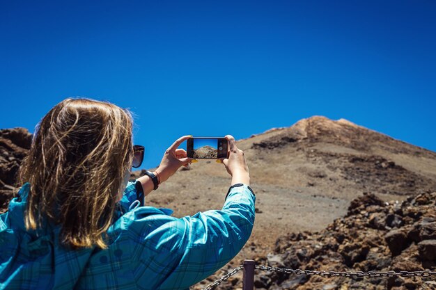 Jonge vrouw die een foto maakt met haar telefoon van een geweldig berglandschap op Tenerife, Canarische eilanden, Spanje Reisconcept