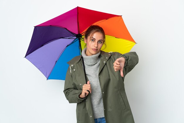 Jonge vrouw die een geïsoleerde paraplu houdt die duim met negatieve uitdrukking toont