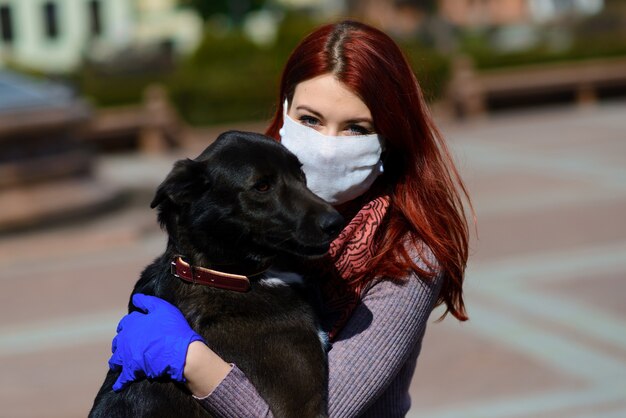 Jonge vrouw die een gezichtsmasker gebruikt als een coronavirus-preventie die met haar hond loopt