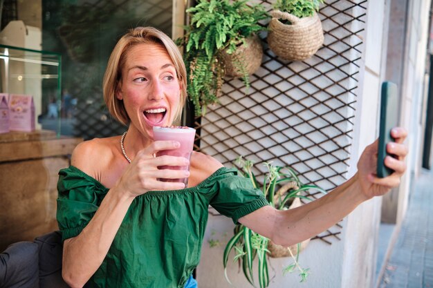 Jonge vrouw die een gezonde smoothie drinkt en doet alsof voor sociale media