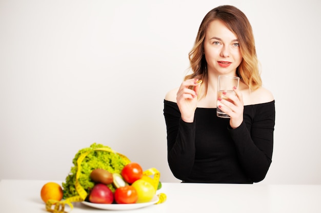 Jonge vrouw die een glas water en een pil voor gewichtsverlies houdt