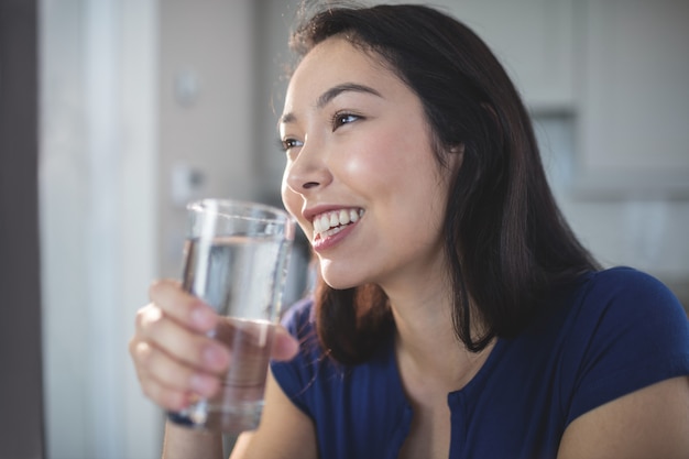 Jonge vrouw die een glas water in keuken drinkt