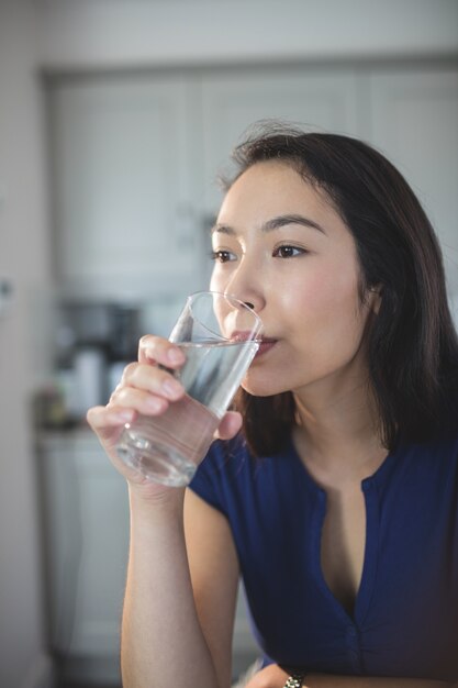 Jonge vrouw die een glas water in keuken drinkt