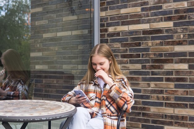 Jonge vrouw die een grappig bericht op de telefoon leest terwijl ze aan een cafetariatafel zit