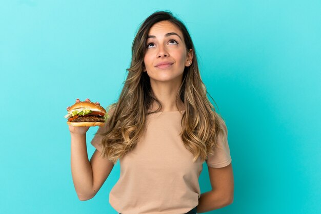 Jonge vrouw die een hamburger over geïsoleerde achtergrond houdt en omhoog kijkt