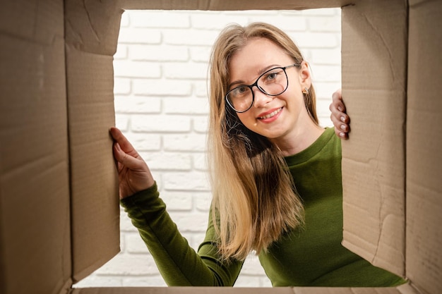 Foto jonge vrouw die een kartonnen doos opent en naar binnen kijkt pakket uitpakken