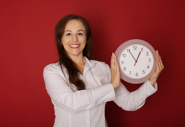 Jonge vrouw die een klok op een rood houdt.