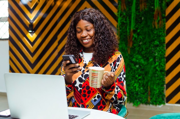 Jonge vrouw die een koffiemok vasthoudt en de telefoon gebruikt in een café