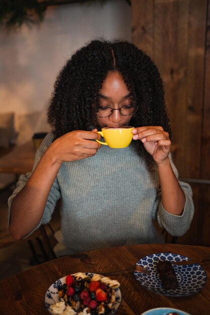 Jonge vrouw die een kopje koffie drinkt in een cafetaria. Ze heeft een brunch