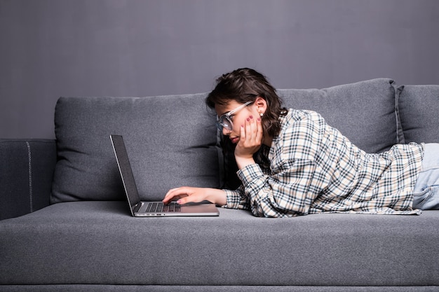 Jonge vrouw die een laptop gebruikt terwijl ze ontspant op de bank