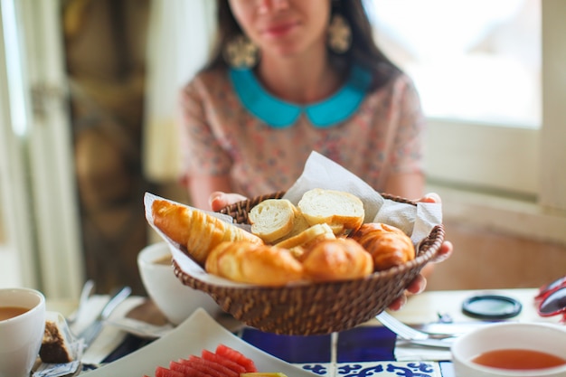 Jonge vrouw die een mand croissants houdt bij het strandrestaurant