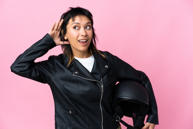 Jonge vrouw die een motorfietshelm over roze muur houdt luisterend iets