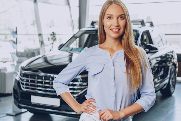 Jonge vrouw die een nieuwe auto controleert die zij in autosalon gaat kopen