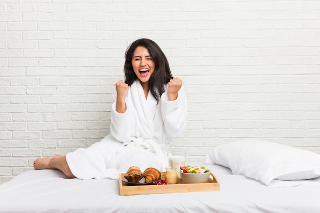 Jonge vrouw die een ontbijt op het bed neemt die onbezorgd en opgewekt toejuichen.