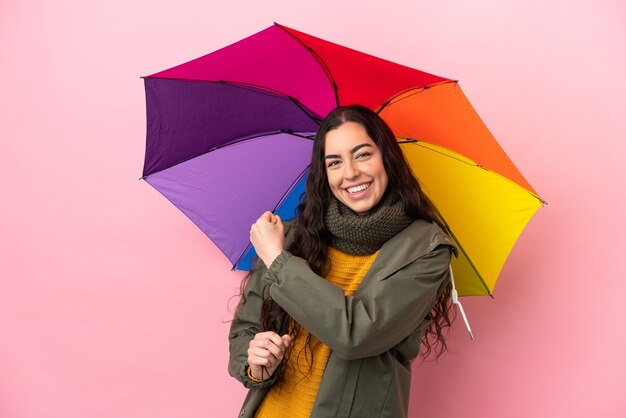 Jonge vrouw die een paraplu houdt die op roze achtergrond wordt geïsoleerd die een overwinning viert