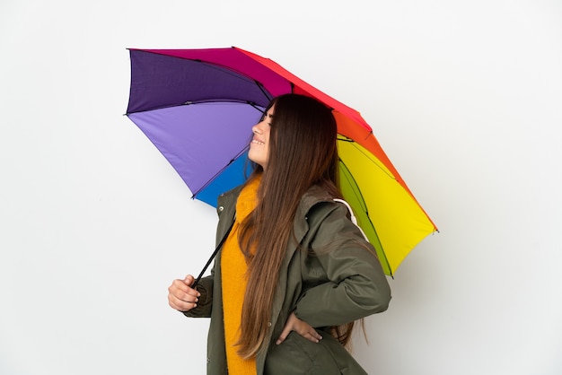 Jonge vrouw die een paraplu houdt die op witte achtergrond wordt geïsoleerd die aan rugpijn lijdt omdat zij zich heeft ingespannen