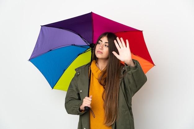 Jonge vrouw die een paraplu houdt die op witte muur wordt geïsoleerd die eindegebaar maakt en teleurgesteld