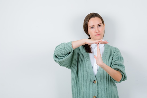 Jonge vrouw die een pauzegebaar in blouse, vest toont en er serieus uitziet, vooraanzicht.